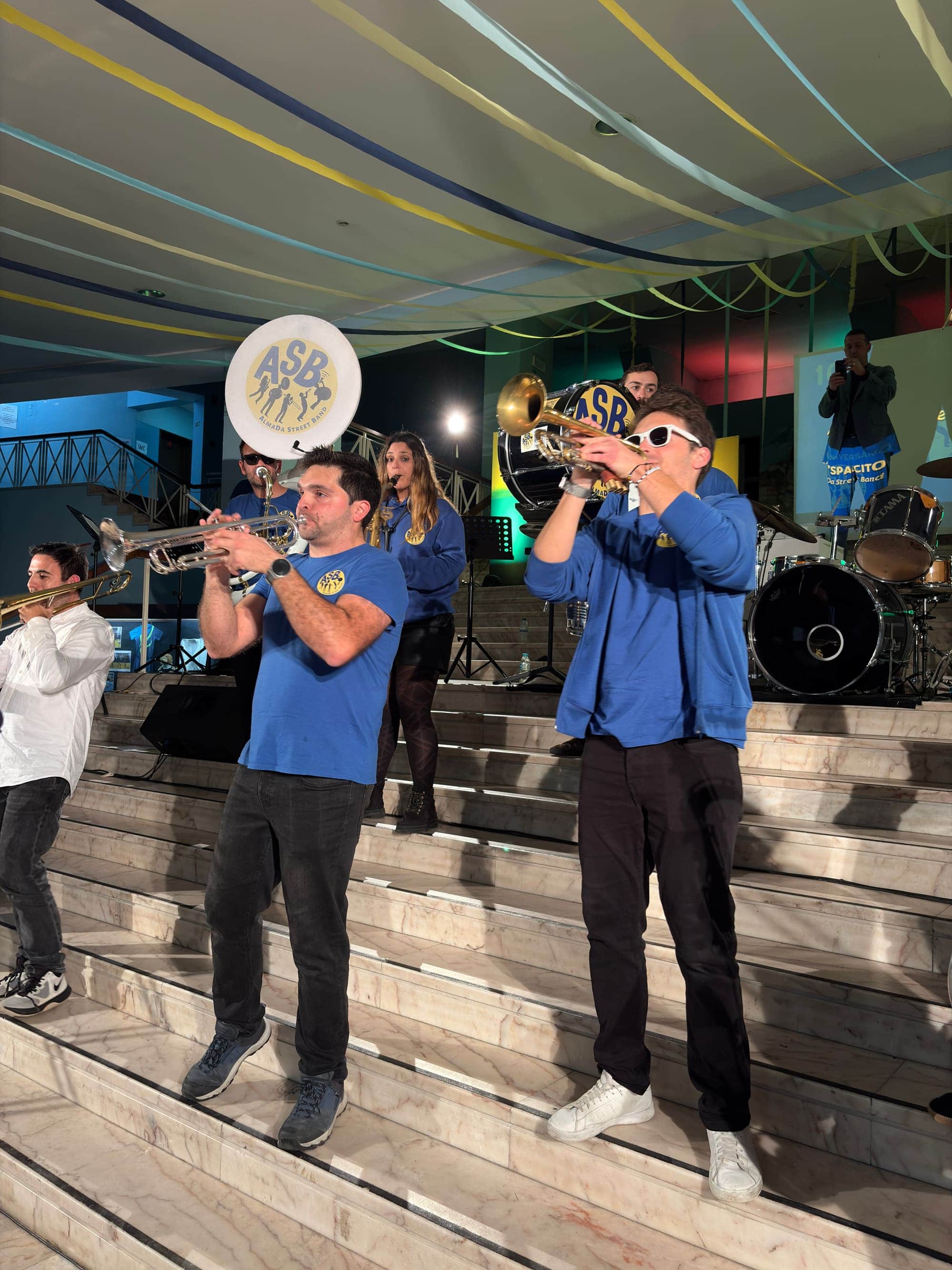 Dois trompetistas a tocar num átrio, em cima de escadas, sob luzes de palco