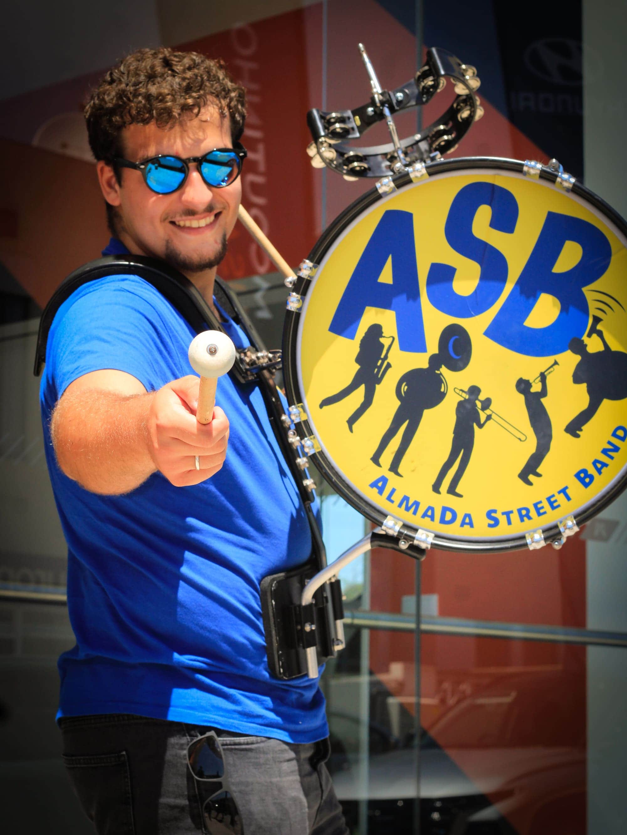 Percussionista a sorrir e a apontar a baqueta à câmara, ao lado do bombo da ASB