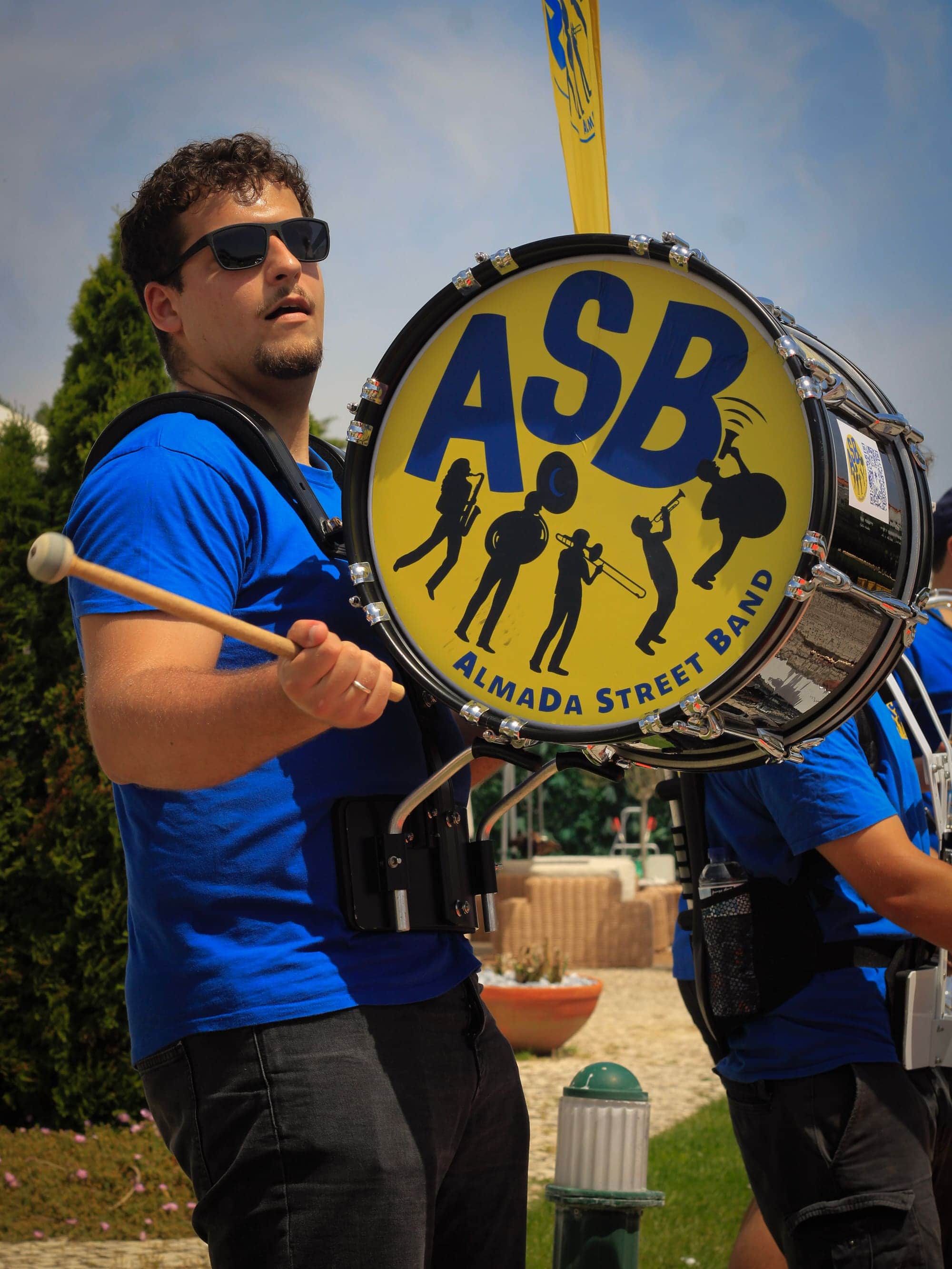Percussionista de óculos escuros com a baqueta erguida junto ao bombo da ASB